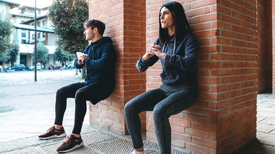 Un hombre y una mujer haciendo sentadillas contra un muro