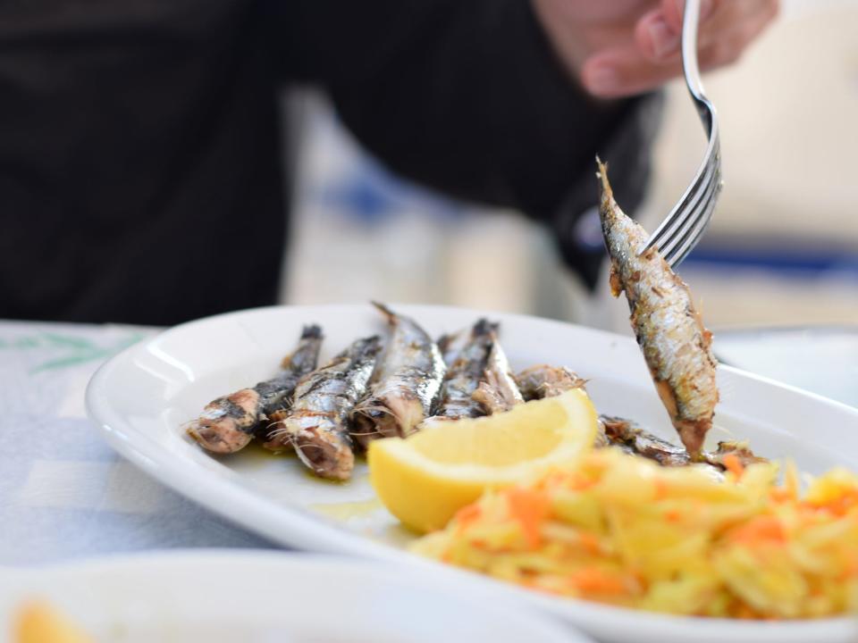 a fork spearing a grilled sardine off a dish of small fish, citrus, and grains