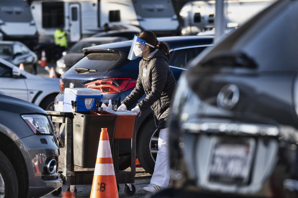 A health care worker gets ready to distribute the COVID-19 vaccine to residents waiting in their cars in the early morning at Dodger Stadium, Tuesday, Jan. 26, 2021, Los Angeles. California is revamping its vaccine delivery system to give the state more control over who gets the shots following intense criticism of a slow and scattered rollout by counties. (AP Photo/Richard Vogel)