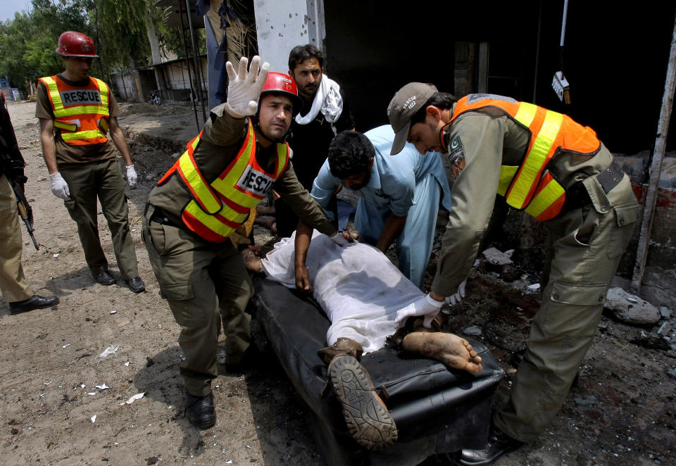 Pakistani rescue workers try to remove the lifeless body of a man killed from a bomb explosion in Peshawar, Pakistan, Sunday, May 11, 2014. A police official in Pakistan says a bomb blast targeting refugees registering with the government has killed several people in northwestern city of Peshawar. Faisal Mukhtar says the bombing Sunday on a soccer field also wounded many people. He says it happened as officials registered refugees from the nearby Khyber tribal region. (AP Photo/Mohammad Sajjad)