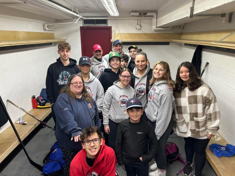 Linda Matteo, pictured here wearing a black jacket and a grey hoodie and surrounded by a host of coaches and volunteers, says many families depend on the Avalanche Kidz Hockey program. 