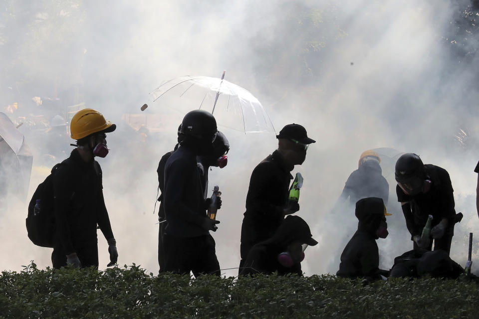 FILE - In this Sunday, Nov. 17, 2019, file photo, pro-democracy protestors react as police fire tear gas at Hong Kong Polytechnic University in Hong Kong. By day, the small commercial kitchen in a Hong Kong industrial building produces snacks. At night, it turns into a secret laboratory assembling a detox kit to help frontline pro-democracy protesters counter ill-effects from repeated exposure to tear gas. (AP Photo/Kin Cheung, File)