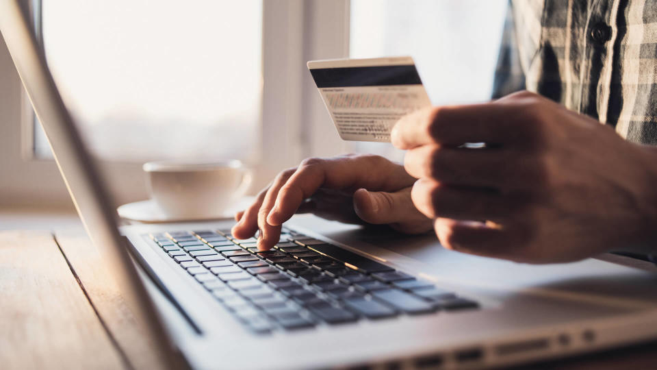 Man holding credit card and using laptop.