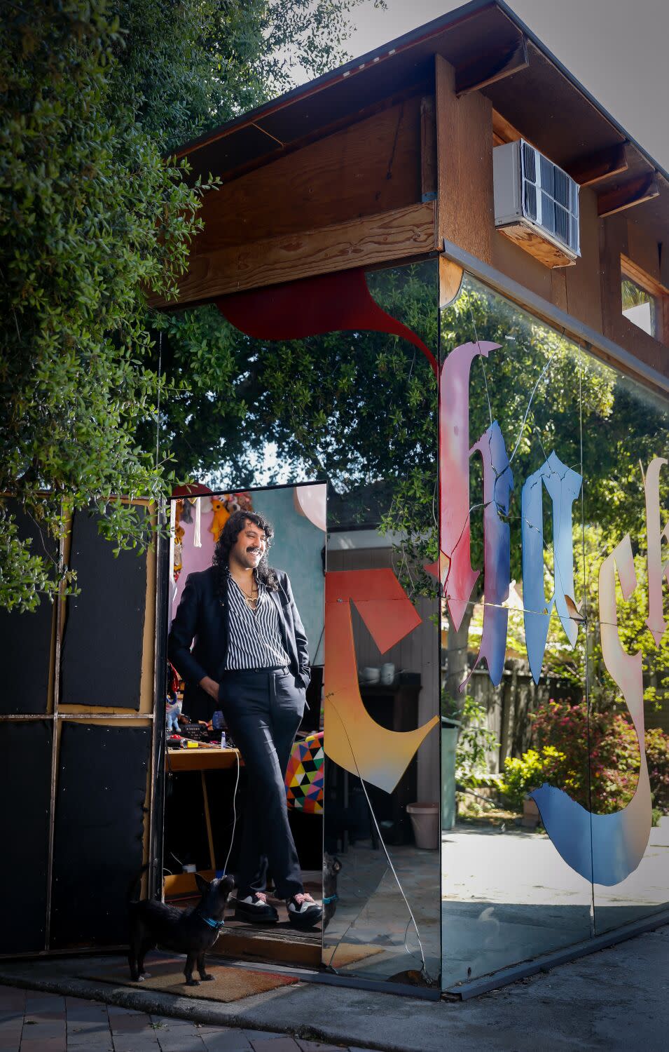 DJ Escuby (Enrique Tena Padilla) is framed by the doorway of a cube covered in mirrors and bearing Old English letters