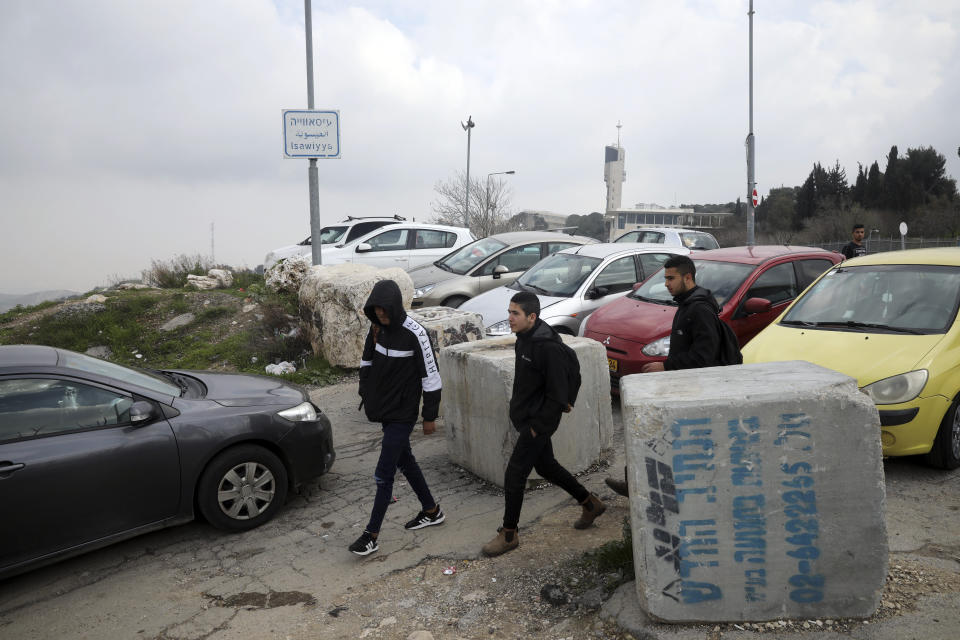 This Monday, Feb. 24 2020 photo, shows Palestinian students passing a roadblock at the entrance to the Palestinian neighborhood of Issawiya in East Jerusalem. Nearly every day for the last nine months Israeli police have stormed into Issawiya in a campaign they say is needed to maintain law and order. Rights groups say that in addition to searching houses and issuing fines, they have detained hundreds of people — some as young as 10, on suspicion of stone-throwing. The operations frequently ignite clashes, with local youths throwing rocks and firebombs. Residents and human rights groups say the provocative raids have created an atmosphere of terror, with parents afraid to let their children play outside. (AP Photo/Mahmoud Illean)