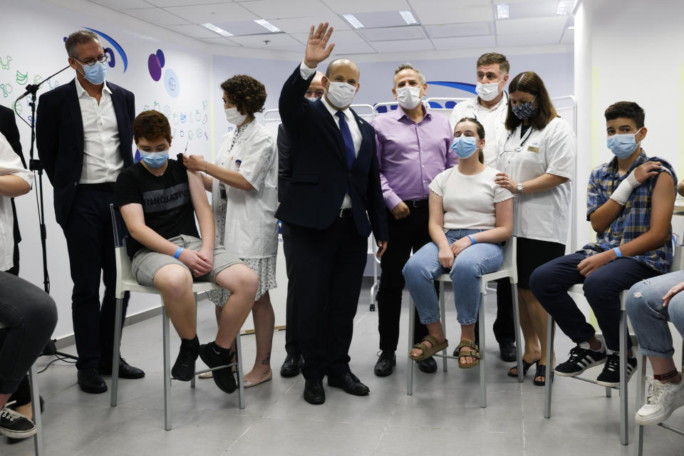 FILE - Israeli Prime Minister Naftali Bennett, center, gestures as he stands next to youths during his visit to a Maccabi healthcare maintenance organisation (HMO) outlet which offers vaccinations against the coronavirus disease (COVID-19) in Holon, near Tel Aviv, Israel Tuesday, June 29, 2021. The coronavirus's omicron variant kept a jittery world off-kilter Wednesday Dec. 1, 2021, as reports of infections linked to the mutant strain cropped up in more parts of the globe, and one official said that the wait for more information on its dangers felt like “an eternity.” (Amir Cohen/Pool Photo via AP, File)