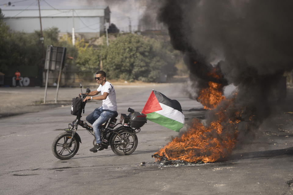 A protester rides his bicycle through burning tires during clashes with the Israeli border police following a demonstration in solidarity with the Gaza Strip, in the West Bank city of Ramallah, Friday, Oct. 20, 2023. (AP Photo/Nasser Nasser)