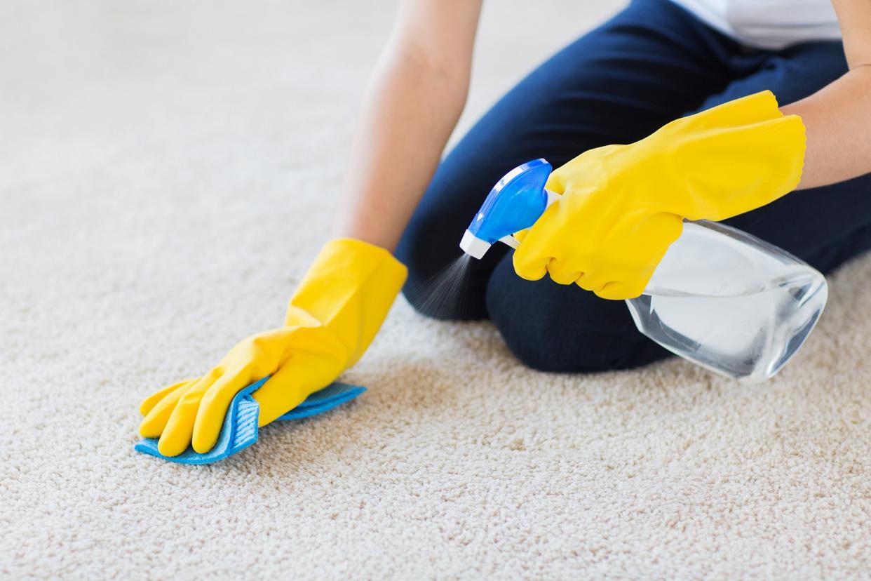 woman in rubber gloves with cloth and detergent spray cleaning carpet at home