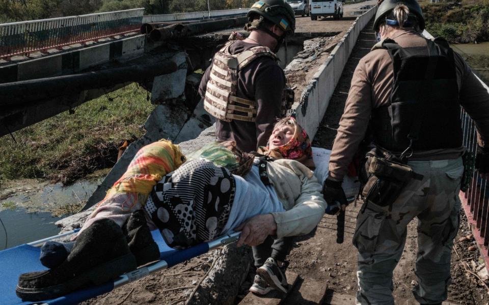 Dusya, 86, is carried on a stretcher by volunteers to cross the broken bridge over the Oskil River in Kupiansk, Kharkiv region - Yasuyoshi CHIBA / AFP