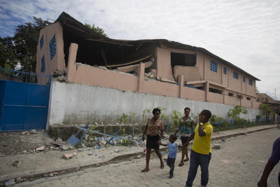 Residents walk past a school damaged by a magnitude 5.9 earthquake the night before, in Gros Morne, Haiti, Sunday, Oct. 7, 2018. Emergency teams worked to provide relief in Haiti on Sunday after the quake killed at least 11 people and left dozens injured. ( AP Photo/Dieu Nalio Chery)