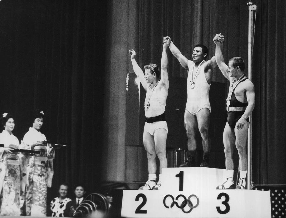 <p>The three winners of the Featherweight Weightlifting event — Isaac Berger of the U.S.A. (silver), Yoshinobu Miyake of Japan (gold) and Mieczyslaw Nowak of Poland (bronze) — raise their hands together on the podium. </p>