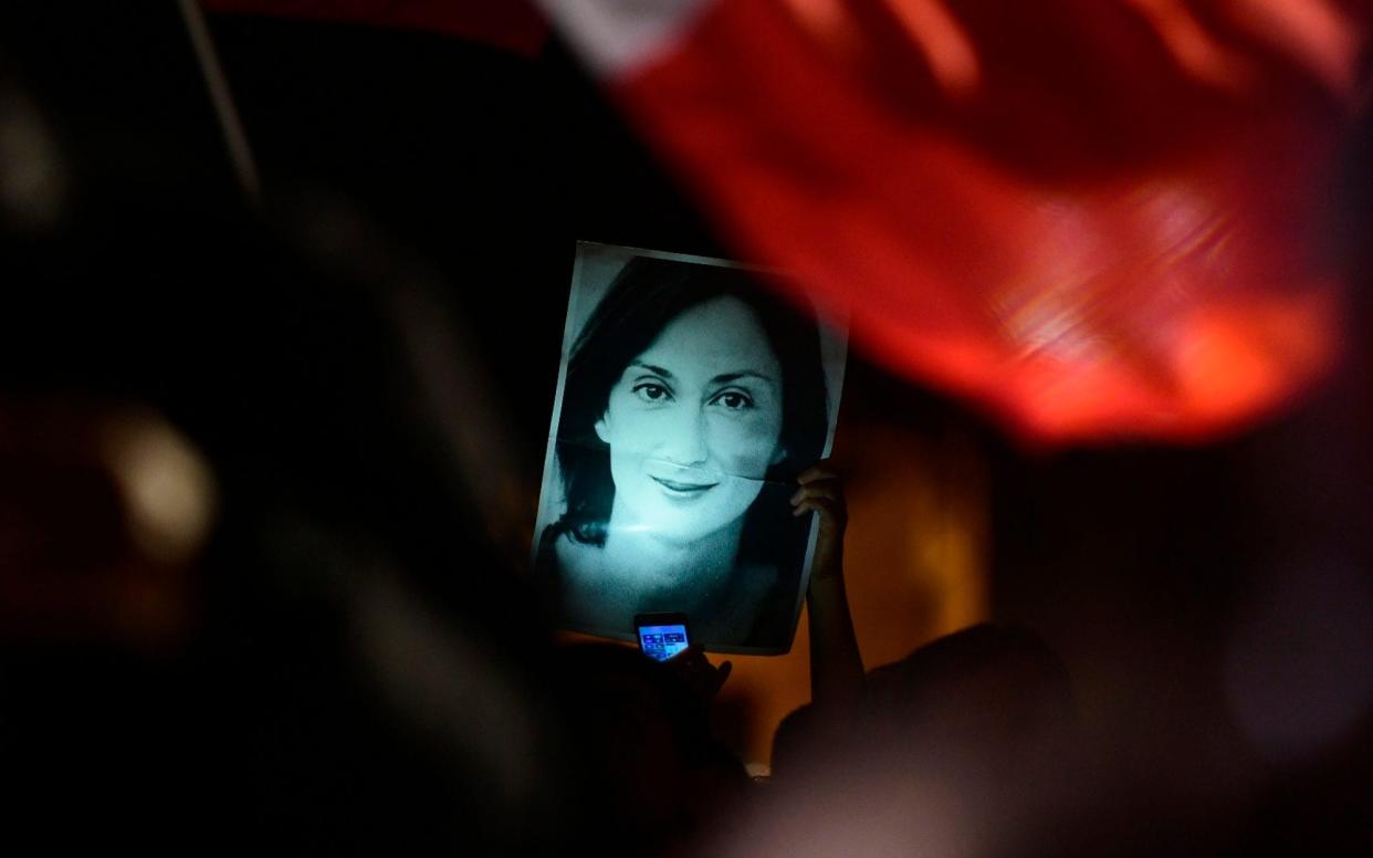 A protester holds up a picture of murdered reporter Daphne Caruana Galizia during a demonstration outside the office of Malta's prime minister's  - AP