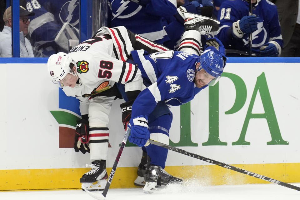 Tampa Bay Lightning defenseman Calvin de Haan (44) checks Chicago Blackhawks right wing MacKenzie Entwistle (58) into the boards during the first period of an NHL hockey game Thursday, Nov. 9, 2023, in Tampa, Fla. (AP Photo/Chris O'Meara)