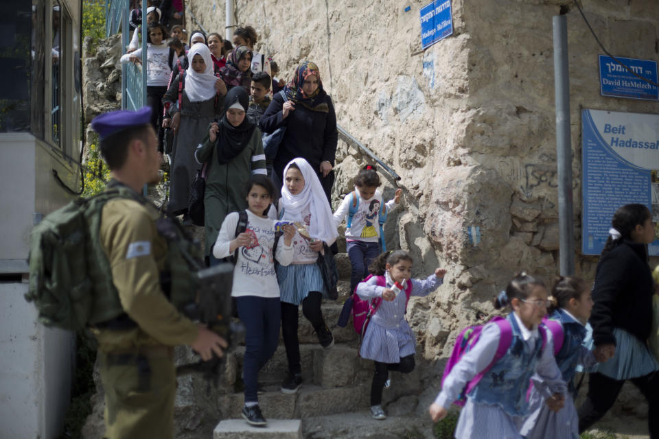 In this March 21, 2019 photo, an Israeli solider stands guard as Palestinian school children cross back from school in the Israeli controlled part of the West Bank city of Hebron. The Falic family, owners of the ubiquitous chain of Duty Free America shops, fund a generous, and sometimes controversial, philanthropic empire in Israel that stretches deep into the West Bank. The family supports many mainstream causes as well as far right causes considered extreme even in Israel. (AP Photo/Ariel Schalit)