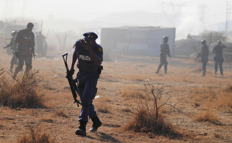 A policeman runs from teargas after police opened fire on striking miners at the Lonmin Platinum Mine near Rustenburg, South Africa, Thursday, Aug. 16, 2012. South African police opened fire Thursday on a crowd of striking workers at a platinum mine, leaving an unknown number of people injured and possibly dead. Motionless bodies lay on the ground in pools of blood. (AP Photo)