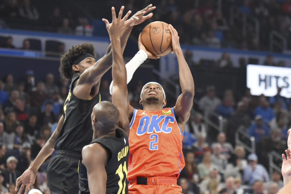 Oklahoma City Thunder guard Shai Gilgeous-Alexander, right, shoots the ball over Utah Jazz forward Taylor Hendricks, left, and guard Kris Dunn, middle, in the first half of an NBA basketball game, Wednesday, Jan. 25, 2023, in Oklahoma City. (AP Photo/Kyle Phillips)