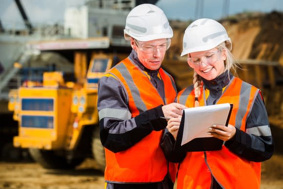 A man and a woman looking at paperwork with a mine truck in the background