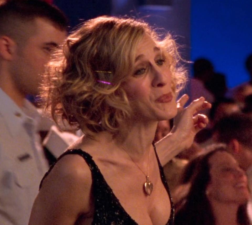 Sarah Jessica Parker, in a sleeveless V-neck dress, at a crowded event. She has wavy short hair adorned with a hair clip