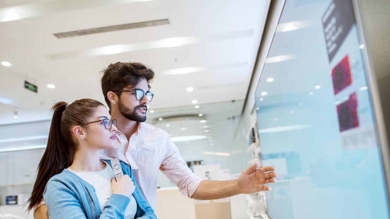 Joyful young attractive multiracial couple checking out plasma TVs in the electronic store.