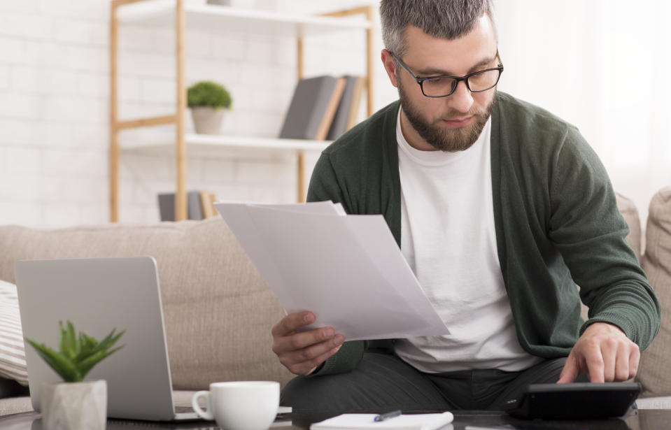 A man wearing a cardigan holding papers and using a calculator