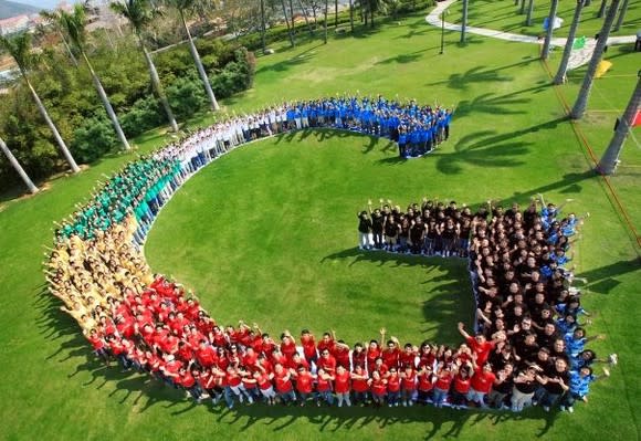 Google employees wearing colored shirts and forming the G logo for Google on a grassy lawn