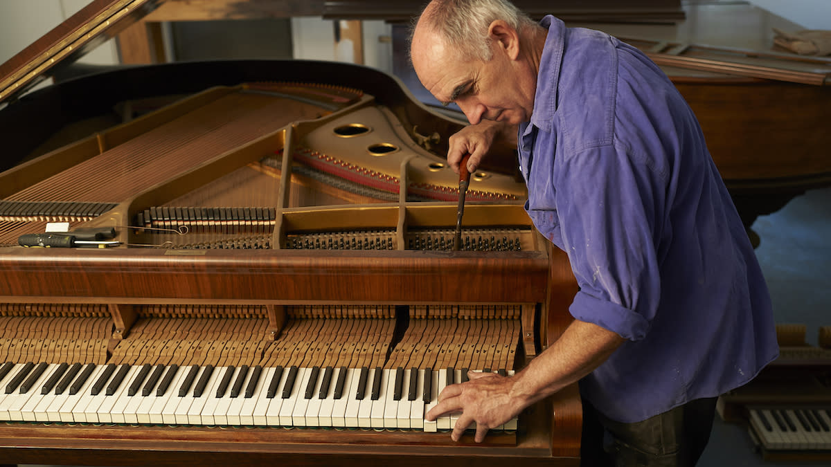  Man in blue shirt tunes an acoustic piano 