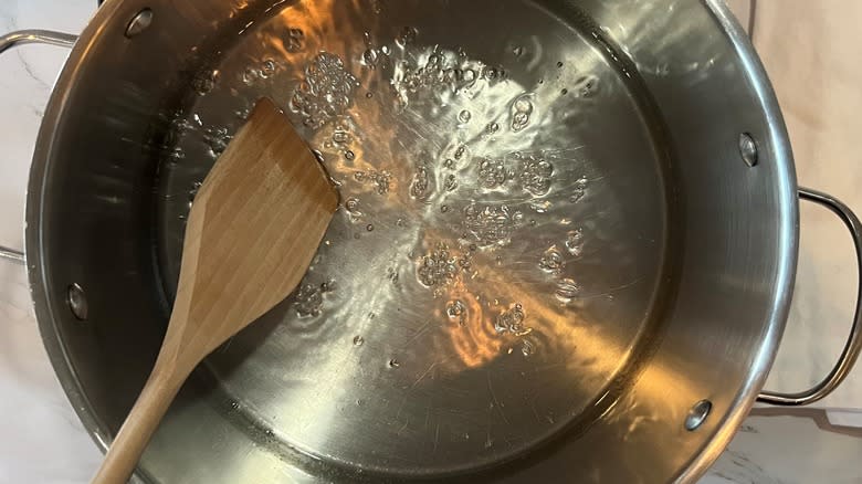 Wooden spoon stirring sugar water in steel pot