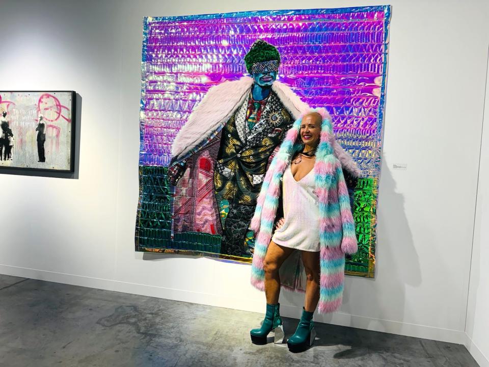 A woman wearing a pastel fur-style coat and sequin minidress poses for a photo in front of a painting.