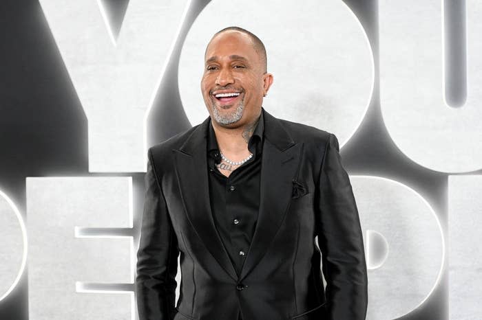 A close-up of Kenya Barris smiling widely at an event for 'You People'. He is wearing a suit and a chain