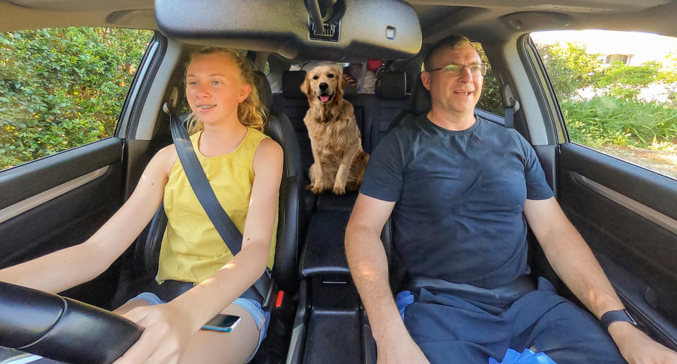 Two people are pictured in a car with a dog in the backseat.