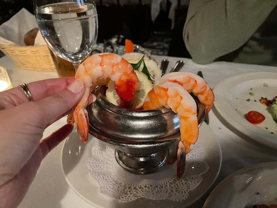 Hand holding shrimp with cocktail sauce on it 