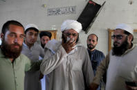 People comfort a cleric who mourns over lost of his students at the site of a bomb explosion in an Islamic seminary, in Peshawar, Pakistan, Tuesday, Oct. 27, 2020. A powerful bomb blast ripped through the Islamic seminary on the outskirts of the northwest Pakistani city of Peshawar on Tuesday morning, killing some students and wounding dozens others, police and a hospital spokesman said. (AP Photo/Muhammad Sajjad)