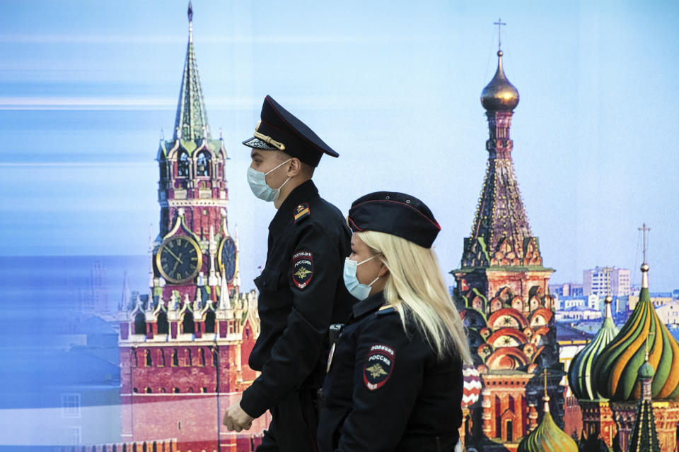 Police officers wearing face masks to protect against coronavirus walk past a photo of Kremlin's Spasskaya Tower, left, and St. Basil's Cathedral in Sheremetyevo Airport, outside Moscow, Russia, Friday, Oct. 9, 2020. The coronavirus outbreak in Russia continues its rapid growth. (AP Photo/Pavel Golovkin)