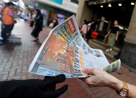 A person takes a newspaper showing the headlines and pictures of the previous night's clashes between police and protesters in front of Wan Chai metro station in Hong Kong