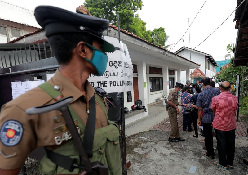 A police officer wearing a protective mask is seen as people wait in a line to cast their vote in Colombo