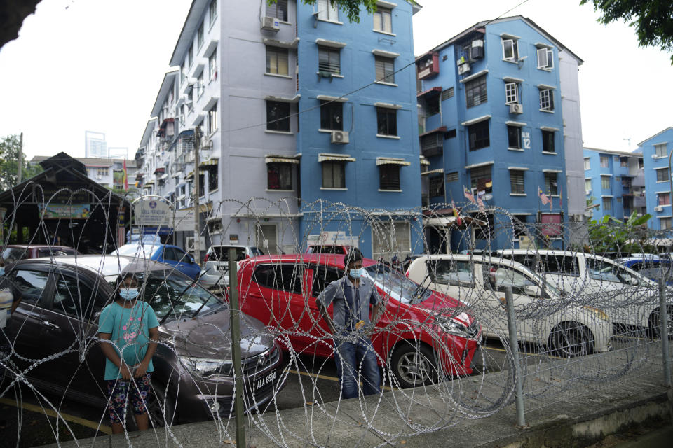 Residents wait for food delivery behind barbwire at Kerinchi area placed under the enhanced movement control order (EMCO) due to drastic increase in the number of COVID-19 cases recorded in Kuala Lumpur, Malaysia, Sunday, July 4, 2021. Malaysia starts further tightening movement curbs and imposes a curfew in most areas in its richest state Selangor and parts of Kuala Lumpur, where coronavirus cases remain high despite a national lockdown last month. (AP Photo/Vincent Thian)