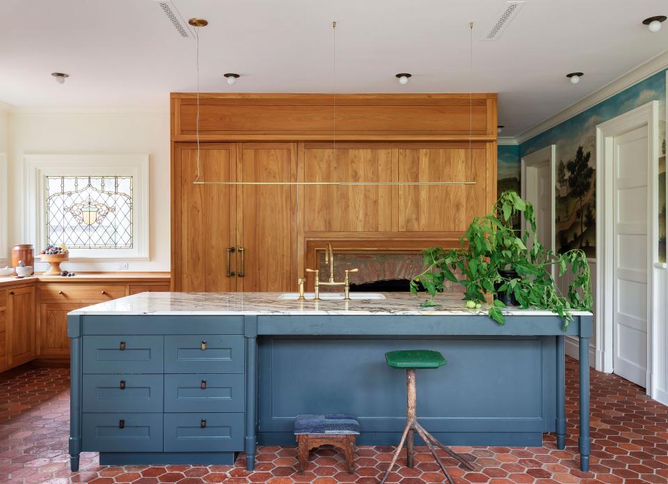 The expansive kitchen juxtaposes peripheral millwork with a central stone-top island and salvaged terra-cotta floor tiles. Markus Bartenschlager made the cabinetry; the knobs are from Pate Woodworks.