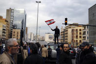 An anti-government protester stands atop his car and waves a national flag as others block a main highway in Beirut, Lebanon, Friday, Jan. 17, 2020. Protesters closed major roads in the capital Beirut and around wide parts of Lebanon paralyzing the country as the political crisis over the formation of a new government worsens. (AP Photo/Bilal Hussein)