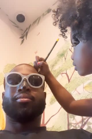 <p>Dwyane Wade/Instagram</p> Dwyane Wade waits patiently as his daughter draws on his face with a pencil as seen on his Instagram Story.