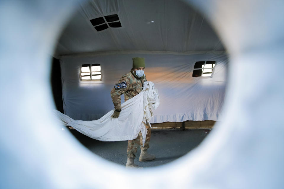 Seen through a metal ventilation tube a Romanian serviceman carries separation panels for a triage tent the army was called to erect outside the Marie Curie children's hospital, in order to separate patients potentially infected with the new Coronavirus before admission, in Bucharest, Romania, Monday, March 16, 2020, as the state of emergency announced last week by the country's president comes into effect. For most people, the new coronavirus causes only mild or moderate symptoms. For some it can cause more severe illness. (AP Photo/Vadim Ghirda)