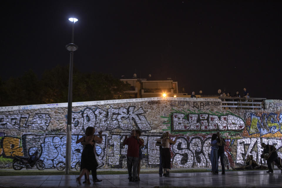 In this Friday, July 26, 2019 photo people dance tango against a stone bridge covered with graffiti in Thission district of Athens. (AP Photo/Petros Giannakouris)