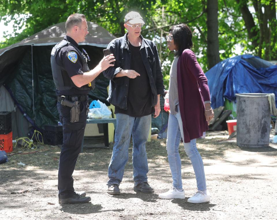 An Akron police officer seeks help Tuesday from homeless advocate Sage Lewis and a member of the homeless camp in identifying a person of interest from a disturbance at a fire station.