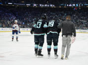 Seattle Kraken left wing Brandon Tanev (13) and a member of the Kraken staff, right, accompany left wing Jared McCann (19) off the ice after McCann was hit into the boards by Colorado Avalanche defenseman Cale Makar during the first period of Game 4 of an NHL hockey Stanley Cup first-round playoff series Monday, April 24, 2023, in Seattle. (AP Photo/Lindsey Wasson)