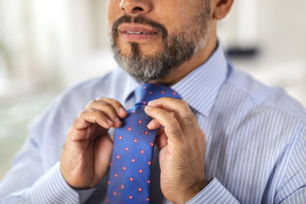 A mature man puts on a blue shirt and tie in front of mirror at home