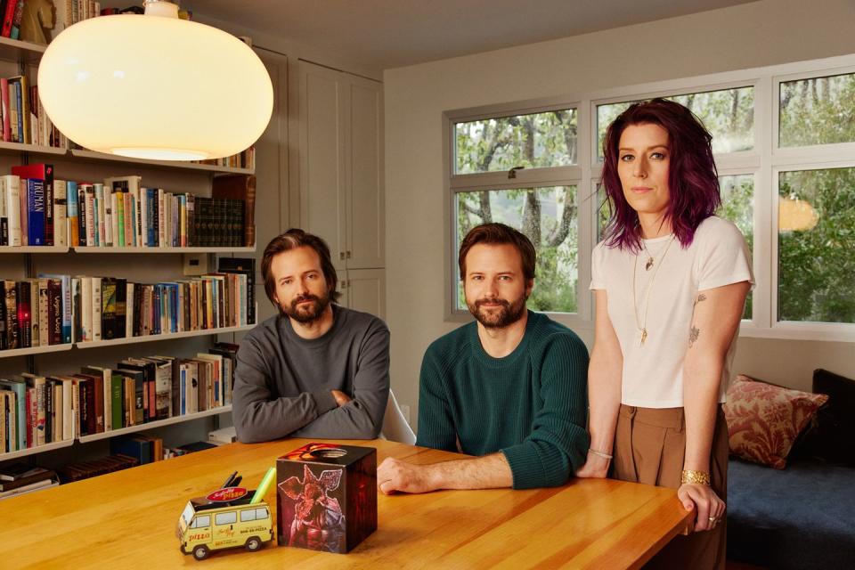 matt duffer, ross duffer, kate trefry sitting and standing at a wooden table