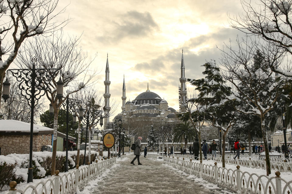 People walk in a snow-covered park with the iconic Haghia Sophia in the background at Istanbul, Tuesday, Jan. 25, 2022. Rescue crews in Istanbul and Athens on Tuesday cleared roads that had come to a standstill after a massive cold front and snowstorms hit much of Turkey and Greece, leaving countless people and vehicles in both cities stranded overnight in freezing conditions. (AP Photo/Emrah Gurel)