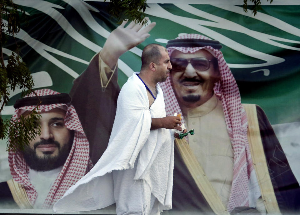 A Lebanese pilgrim walks in front of a banner showing Saudi King Salman, right, and his Crown Prince Mohammed bin Salman, near the Mountain of Mercy, on the Plain of Arafat, during the annual hajj pilgrimage, near the holy city of Mecca, Saudi Arabia, Saturday, Aug. 10, 2019. More than 2 million pilgrims were gathered to perform initial rites of the hajj, an Islamic pilgrimage that takes the faithful along a path traversed by the Prophet Muhammad some 1,400 years ago. (AP Photo/Amr Nabil)