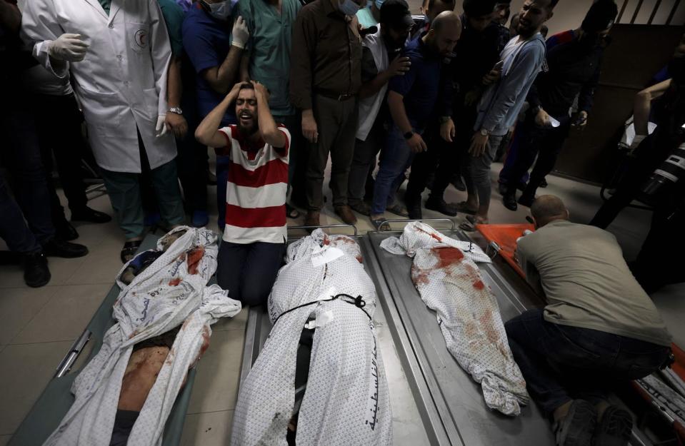 A man in grief on his knees next to the bodies of three of his family members laid out on stretchers.