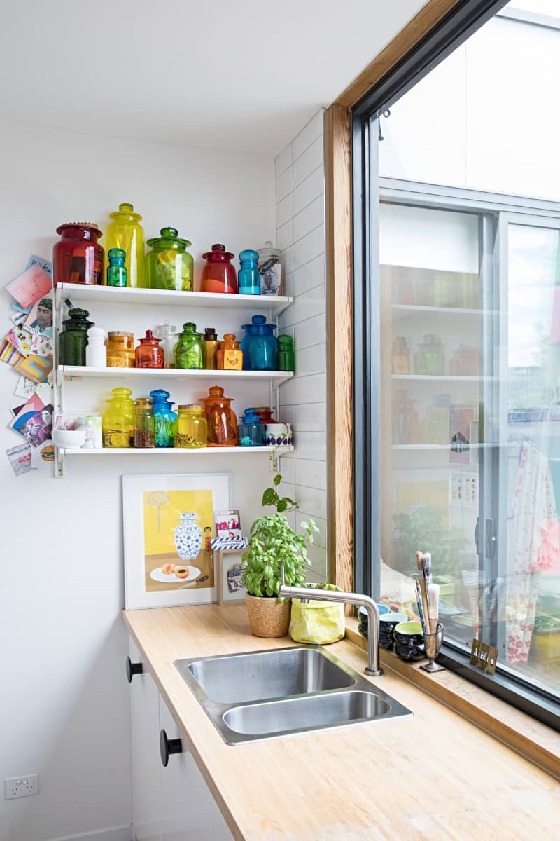 sink below large window with wood counter tops and rainbow glass jars on exposed shelves