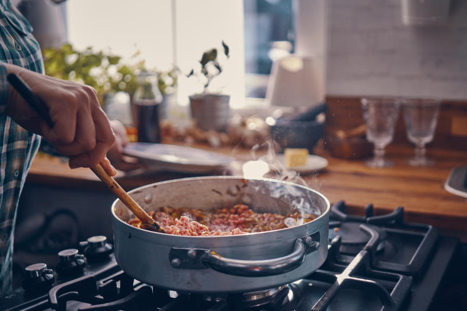 A person stirs a pan of food on a stove in a cozy kitchen setting, suggesting a romantic home-cooked meal scene